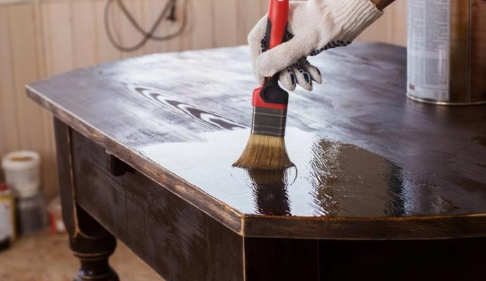 Person applying varnish to wooden table